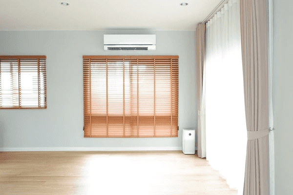 A modern minimalist room with wooden blinds, soft drapes, and an air conditioning unit, creating a balanced mix of natural light and privacy.