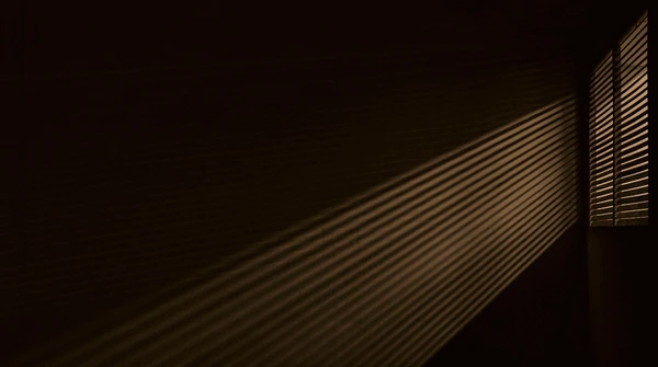 Dramatic light rays passing through window blinds in a dark room, showcasing effective sunlight control and eye strain reduction in Dubai interiors.