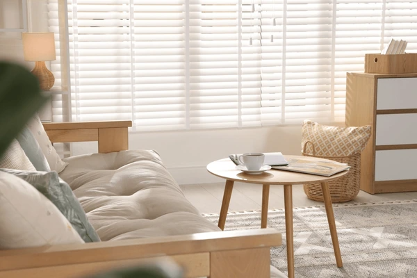 A cozy, sunlit living room with elegant white cut-size blinds, a stylish wooden sofa, and a minimalist coffee table, creating a warm and modern ambiance in Dubai 2025.