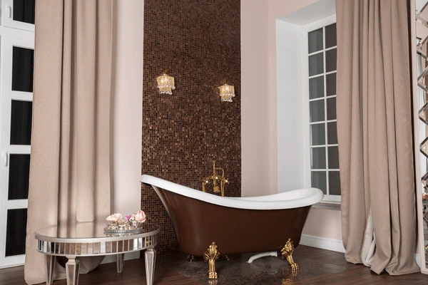 A luxurious bathroom featuring a vintage clawfoot bathtub, rich brown mosaic wall, elegant beige curtains, and opulent gold accents, creating a sophisticated and timeless ambiance.