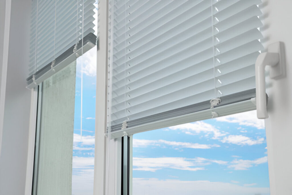 A close-up of white pleated blinds installed on a glass window, partially open to reveal a clear blue sky, blending modern functionality with traditional Emirati aesthetics, making them a trendy and cultural choice for Dubai homes.