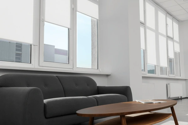 Sleek white window roller blinds in a contemporary living room with a dark grey sofa and wooden coffee table.
