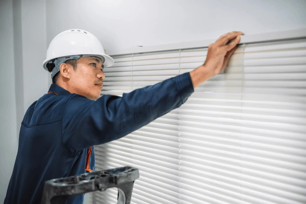 A maintenance worker installing white Venetian blinds, ensuring a secure and professional DIY window treatment setup.