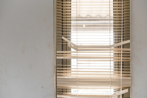 A set of damaged window blinds with several broken and bent slats, letting in sunlight through the gaps.