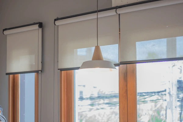A stylish interior featuring white roller blinds over wooden-framed windows, complemented by a modern pendant light, creating a luxurious and elegant ambiance in Dubai 2025.