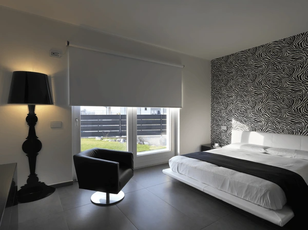Modern Dubai bedroom with blackout roller blinds, monochrome décor, leather chair, and zebra-print accent wall.