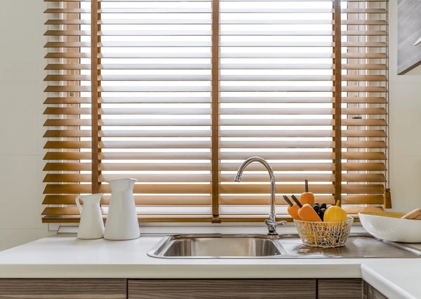 Warm wooden blinds above a modern kitchen sink in a Dubai home, with fruit basket and minimal countertop decor.