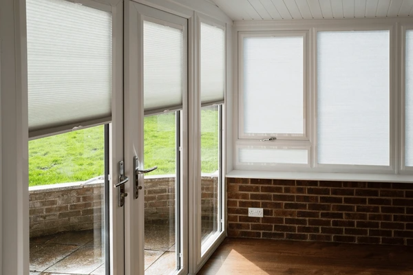 A modern conservatory with sleek, made-to-measure white blinds covering large windows and glass doors.