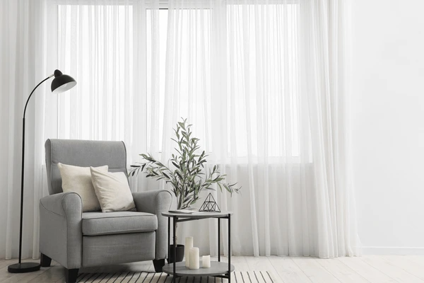 Cozy living room corner with a gray armchair, black floor lamp, and sheer white luxurious curtains, ideal for modern Dubai homes.