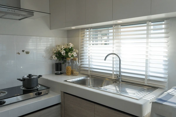 Dubai kitchen 2025 with white horizontal blinds, stainless steel sink, neutral-toned cabinets, and soft overhead lighting for a modern vibe.