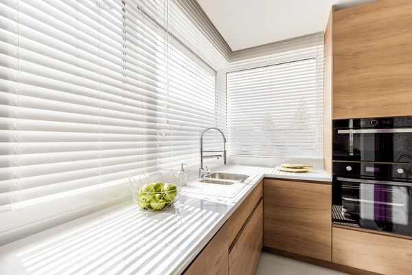 A stylish Dubai kitchen in 2025 featuring white horizontal blinds, wooden cabinets, and a sleek countertop with bright natural lighting.