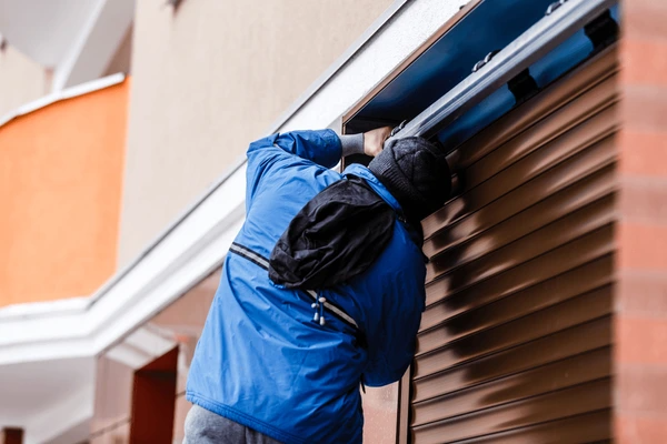 Technician in blue jacket repairing an outdoor roller shutter on a modern Dubai apartment building.