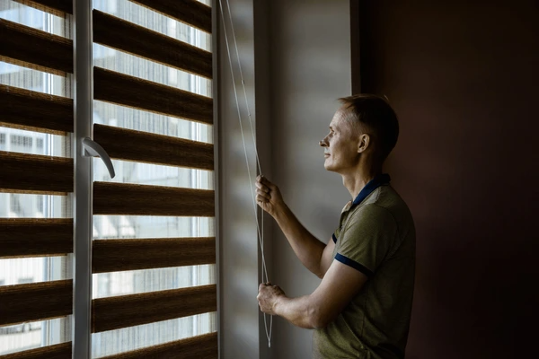 Man pulling the cord of modern roller blinds in a stylish, cozy room in Dubai 2025