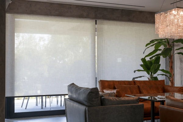 Modern living room in Dubai featuring large windows with elegant white soundproof roller blinds and stylish leather furniture.