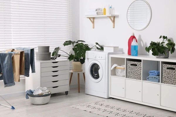 Stylish laundry room in Dubai with sleek white blinds, washing machine, modern storage, indoor plants, and drying clothes.