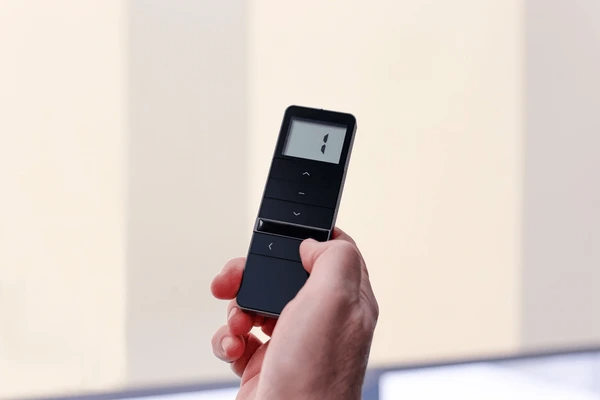 A person holds a smart remote to control motorized blinds in a modern Dubai home with soft ambient lighting.
