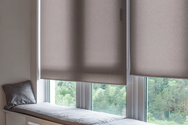 Close-up of modern motorized roller blinds over large windows with a cushioned bench and pillow, creating a cozy and elegant setting in Dubai, 2025.