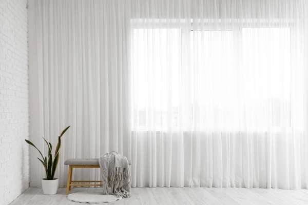 Bright room with sheer anti-condensation and moisture-resistant curtains, a potted plant, a bench, and a cozy throw in Dubai.