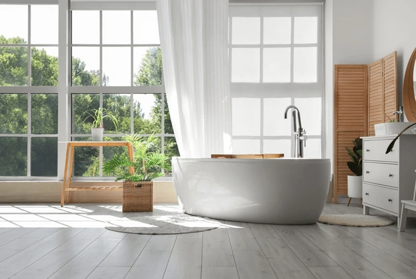 Elegant white bathroom with large windows, a freestanding tub, and moisture-resistant white curtains filtering sunlight.