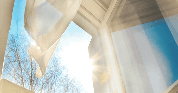 Open window with sunlight streaming through a light, sheer curtain blowing in the breeze, ideal for maintaining cool indoor temperatures in Dubai.