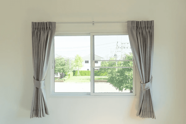Minimalist window with tied-back light grey thermal curtains in a modern room, offering a clear outdoor view.