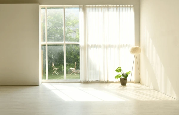 Best Drop Curtains in Dubai 2025 - Light, airy curtains over a large window, bringing natural light into a cozy living room with a plant and modern furniture.