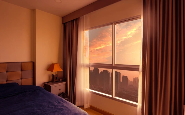 Best Drop Curtains in Dubai 2025 - Elegant curtains framing a beautiful sunset view from a modern bedroom with a sleek bed and stylish lamp.