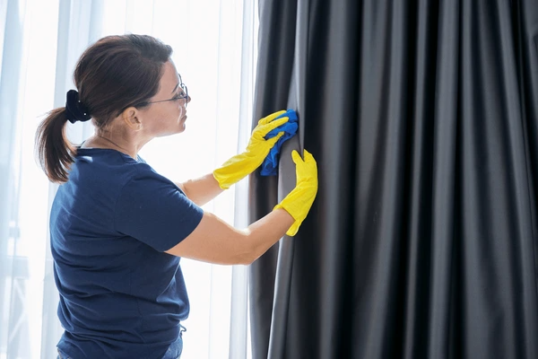 A woman cleaning easy-to-clean wave curtains in a modern living room, demonstrating the practical and sleek design for Dubai homes in 2025.