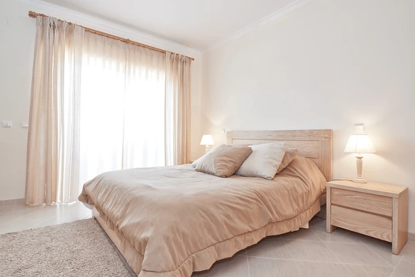 Cozy bedroom with light-colored curtains, providing effective heat protection and a serene atmosphere.