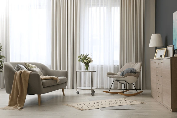 Elegant noise-reducing curtains in a modern Dubai living room with soft furniture, a rocking chair, and natural lighting.