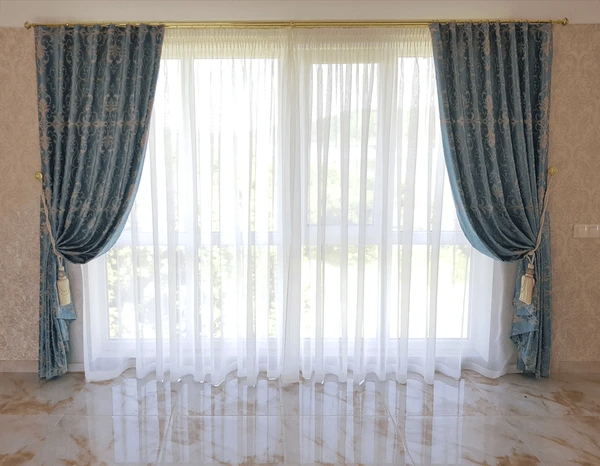 Classic living room with luxurious blue velvet curtains and sheer white drapes over a large window.