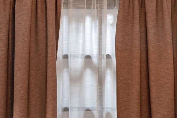 Brown privacy-friendly blackout curtains with sheer white inner layer covering a window for added style and light control.