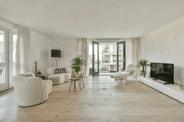 Bright modern living room with white quality curtains, open balcony doors, soft furnishings, and neutral wood flooring.
