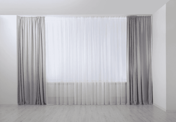  Light grey floor-length curtains paired with white sheers in a bright, modern room with wooden flooring.