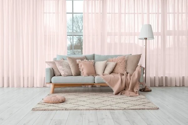 A cozy living room with soft pink shrink-proof curtains and a stylish sofa with plush pillows, creating a luxurious and modern atmosphere.