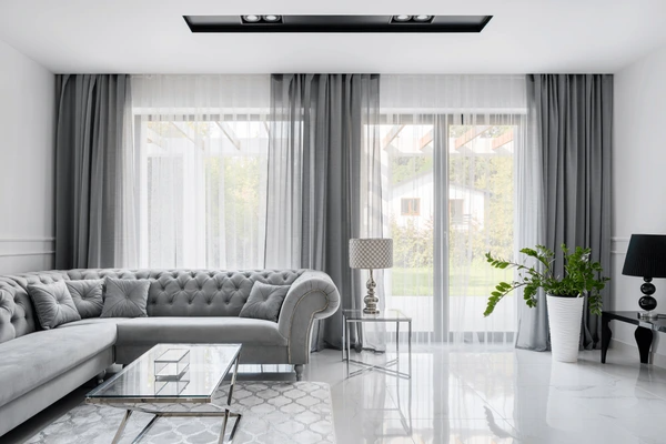 Contemporary living room with sleek grey used curtains, covering large modern glass windows paired with a tufted grey sofa and marble floor.