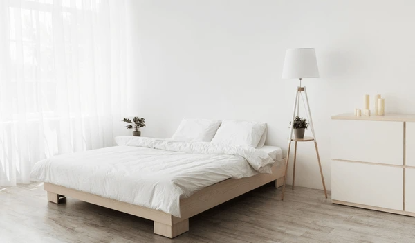 Bright, minimalist bedroom in Dubai with soft, used white sheer curtains filtering daylight through large windows beside a cozy bed.