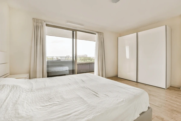 Tall window with soft grey used curtains inside a high-rise apartment, overlooking Dubai's lush residential landscape in daylight.