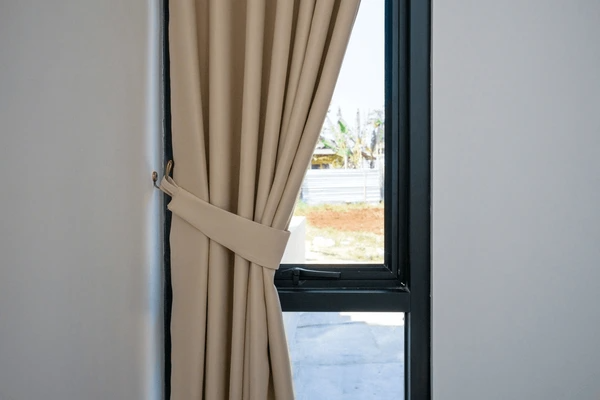 Minimalist beige curtain tied to the side of a modern black-trimmed window, allowing natural light to filter into the room.