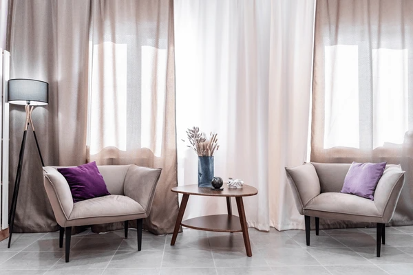 Elegant beige and white curtains behind modern armchairs with purple cushions in a cozy Dubai living room