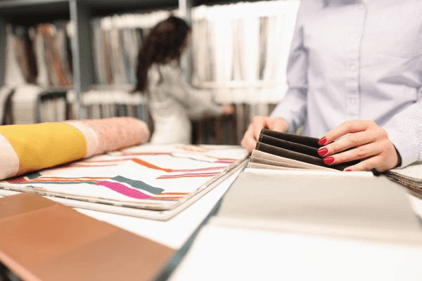 Close-up of a woman’s hands exploring a selection of curtain fabrics in a Dubai showroom, showcasing premium Emirati blinds and curtain materials.