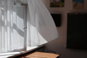 Light sheer white curtain swaying in sunlight through an open window in a bright, minimal room.