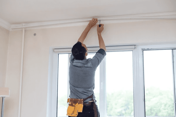 Skilled technician installing a curtain rail system above wide glass windows in a contemporary Dubai home.