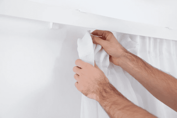 Close-up of a man's hands installing white curtains on a ceiling-mounted track system in a modern Dubai interior.
