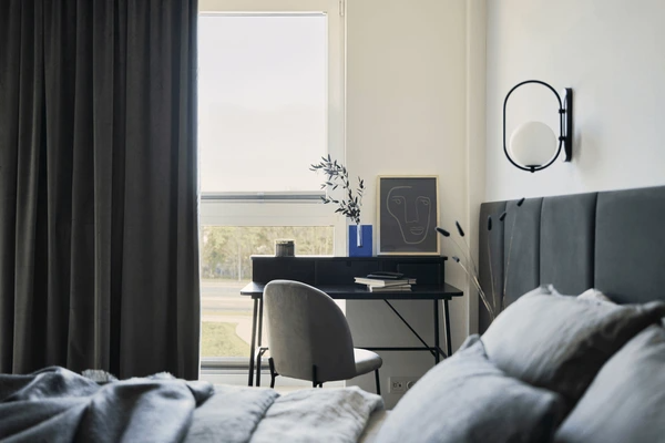 Elegant bedroom interior in Dubai featuring dark blackout curtains, a modern bed, and a small workspace by the window.