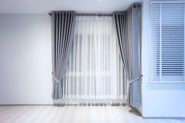 Modern bedroom setup with dual-layered grey curtains and white sheer panels in a minimalist empty room in Dubai.