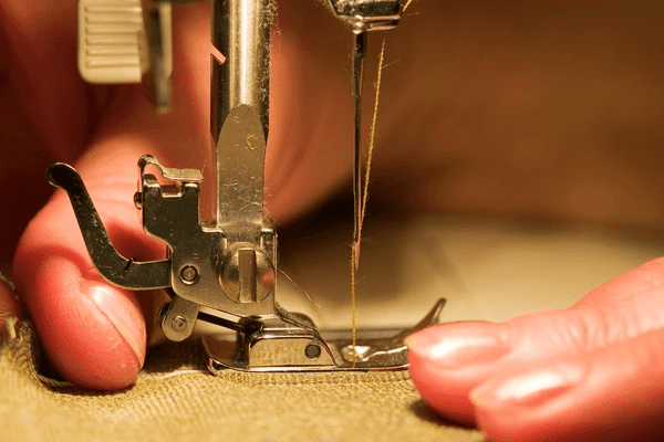 Close-up of hands sewing fabric on a machine, showing expert precision and craftsmanship by a professional curtain maker in Dubai’s luxury interior market.

