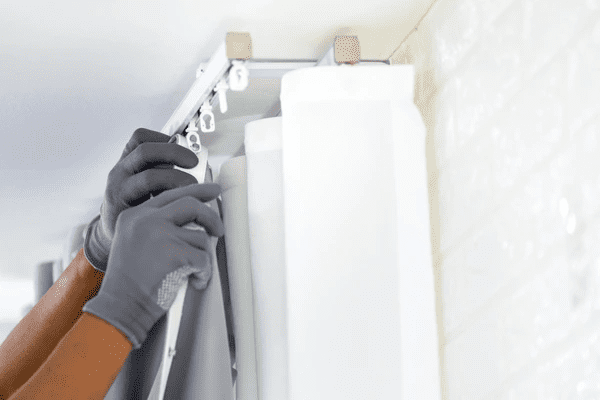 Close-up of a professional in gloves expertly hanging dual-layer curtains on a ceiling-mounted track system in a modern Dubai home.
