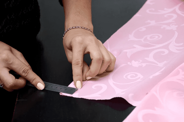 Close-up of a skilled curtain maker’s hands cutting pink patterned fabric with precision, showing expert craftsmanship in custom curtain making in Dubai.

