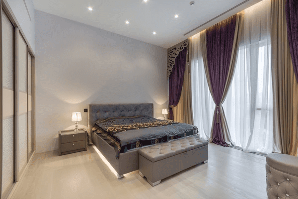 Elegant bedroom featuring rich purple and beige privacy curtains over sliding glass doors in a luxurious Dubai home.